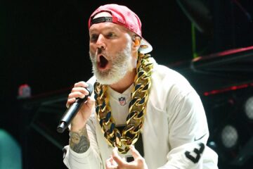 Fred Durst, vocalista do Limp Bizkit, se apresenta ao vivo usando boné vermelho para trás, corrente dourada e camiseta branca.