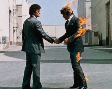 Capa do álbum Wish You Were Here, do Pink Floyd, mostrando dois homens de terno apertando as mãos enquanto um deles está em chamas.