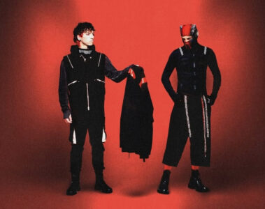 Capa promocional de Breach (2025), álbum do Twenty One Pilots, com Tyler Joseph e Josh Dun em cenário vermelho, explorando a saga de Clancy.