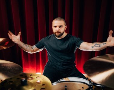 Eloy Casagrande, baterista do Slipknot, posando em seu kit de bateria com cortina vermelha ao fundo, em foto promocional tirada por Estevam Romera.