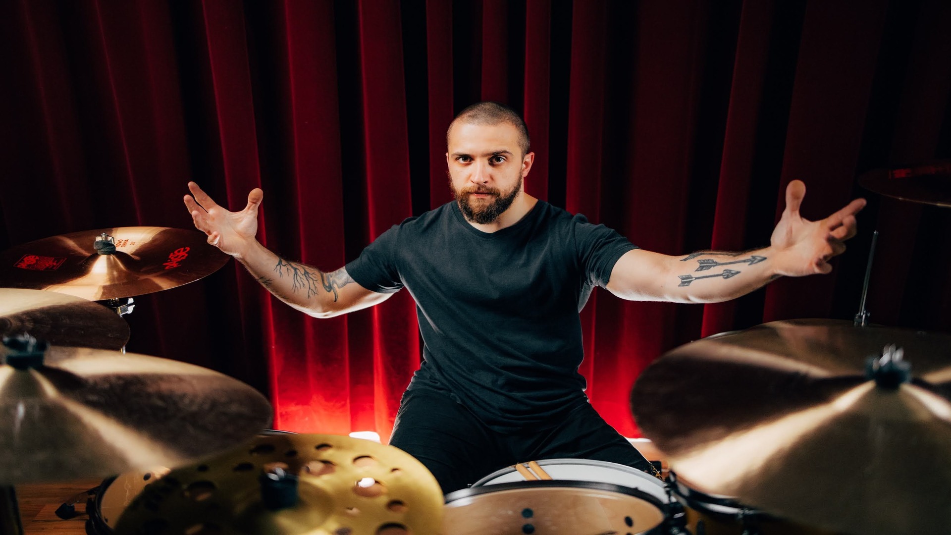 Eloy Casagrande, baterista do Slipknot, posando em seu kit de bateria com cortina vermelha ao fundo, em foto promocional tirada por Estevam Romera.