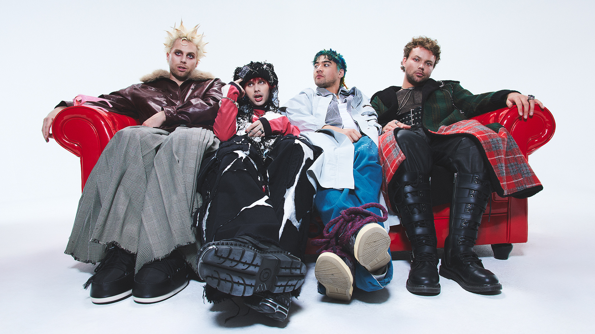A banda 5 Seconds of Summer posa em um sofá vermelho com looks alternativos e atitude descontraída para divulgar o single “Boyband” e o álbum EVERYONE’S A STAR!.