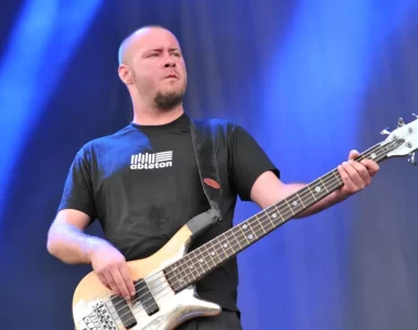 Sam Rivers tocando baixo durante show do Limp Bizkit, com expressão concentrada e fundo azul iluminado.