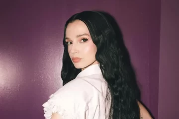 Poppy posa com expressão séria e cabelos longos ondulados diante de uma parede roxa, promovendo seu cover melancólico de “Last Christmas”, do Wham!.