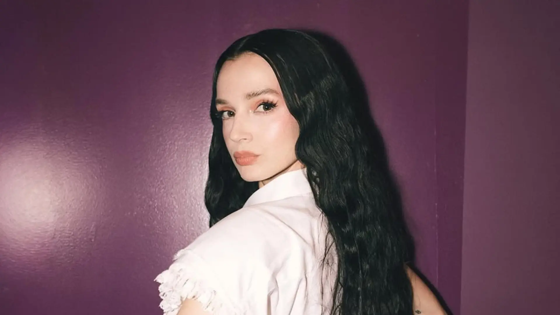 Poppy posa com expressão séria e cabelos longos ondulados diante de uma parede roxa, promovendo seu cover melancólico de “Last Christmas”, do Wham!.