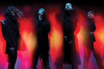 A banda Korn em imagem promocional da turnê Latin America 2026, com visual sombrio e iluminação vermelha e laranja intensa.
