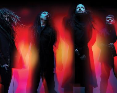 A banda Korn em imagem promocional da turnê Latin America 2026, com visual sombrio e iluminação vermelha e laranja intensa.