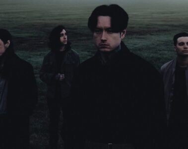 Banda Bad Omens em foto promocional no campo, com Noah Sebastian em primeiro plano; crédito de Bryan Kirks.