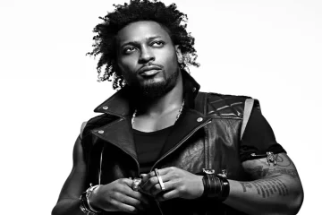 Retrato em preto e branco de D’Angelo usando jaqueta de couro, olhando para o lado com expressão séria.