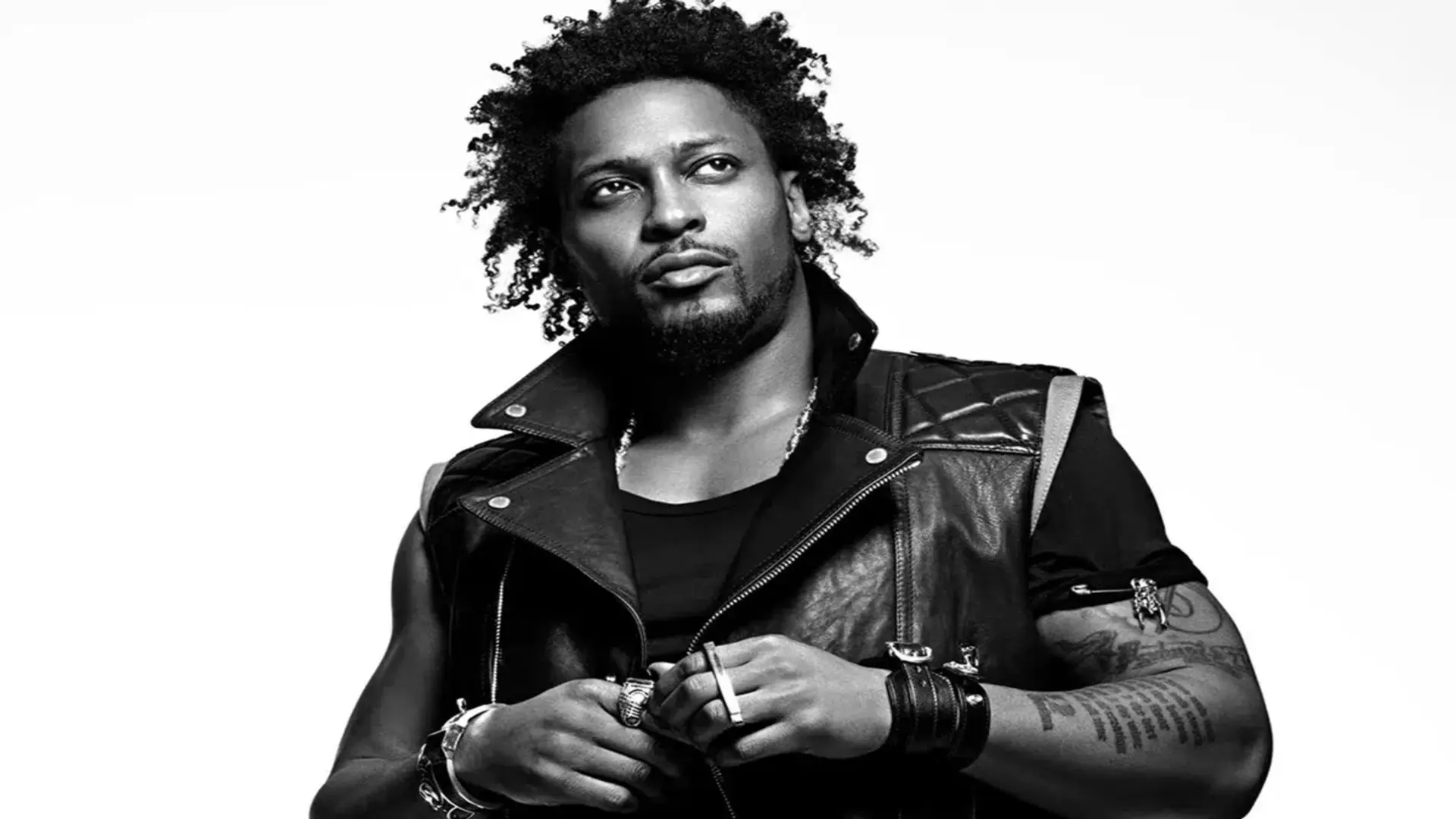 Retrato em preto e branco de D’Angelo usando jaqueta de couro, olhando para o lado com expressão séria.