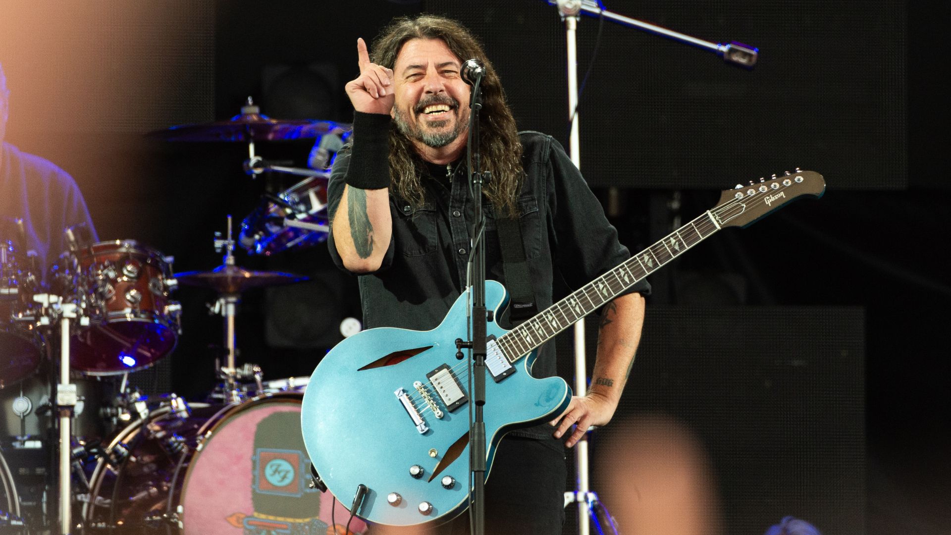 Dave Grohl sorrindo e apontando para cima enquanto toca guitarra azul em show do Foo Fighters.