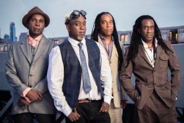 Integrantes da banda Living Colour posam juntos em ambiente urbano durante sessão promocional da turnê “The Best of 40 Years”.