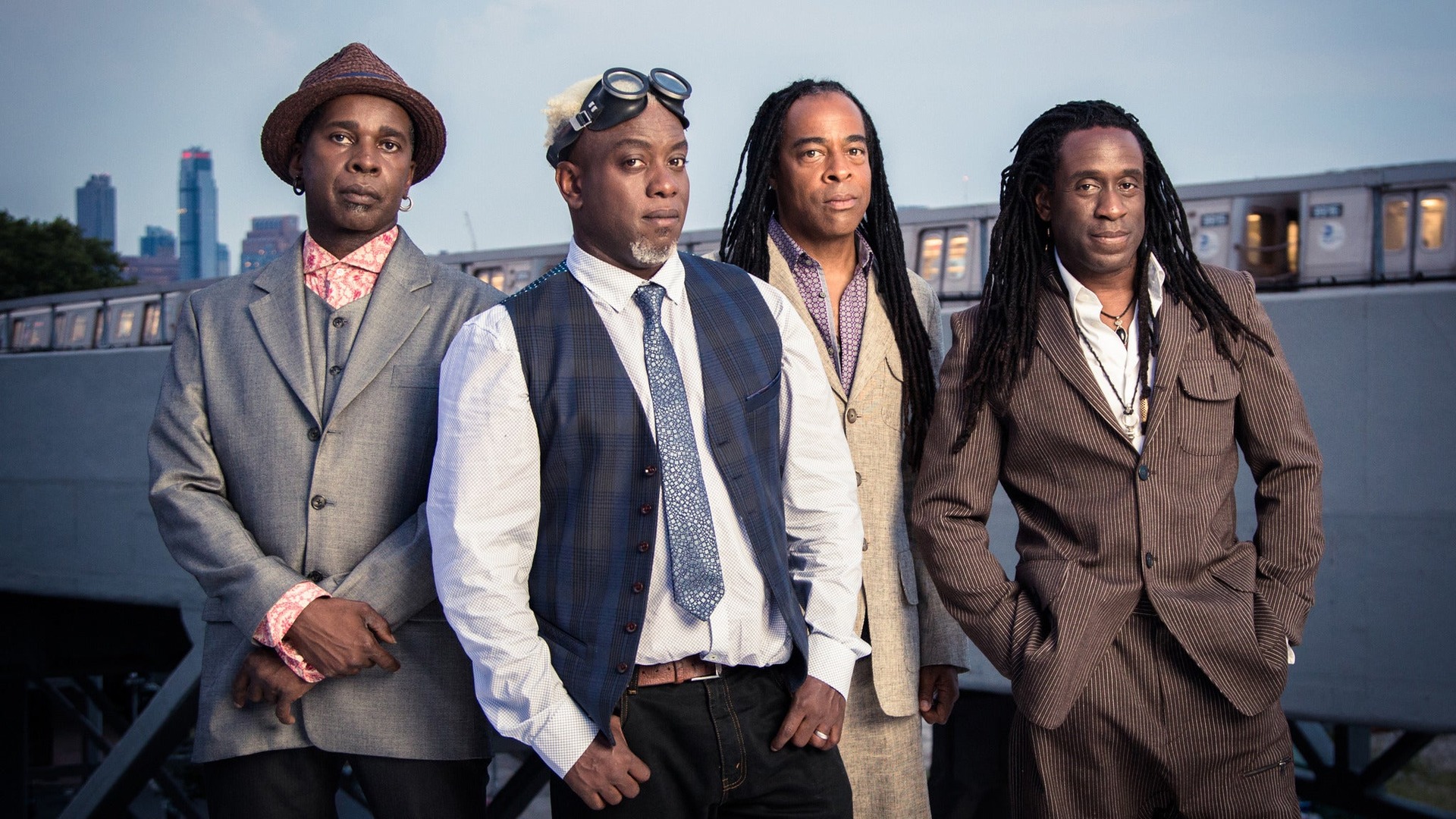 Integrantes da banda Living Colour posam juntos em ambiente urbano durante sessão promocional da turnê “The Best of 40 Years”.