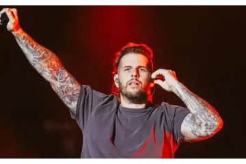 M. Shadows, vocalista do Avenged Sevenfold, canta no palco com braço erguido durante show — imagem promocional da turnê no Brasil em 2026.