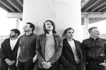 Foto em preto e branco da banda Mayday Parade posando sob um viaduto, divulgando o single “Promises” do álbum Sad (Crédito: Eli Ritter).