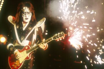 Ace Frehley tocando guitarra durante show do Kiss, com fogos de artifício no palco.