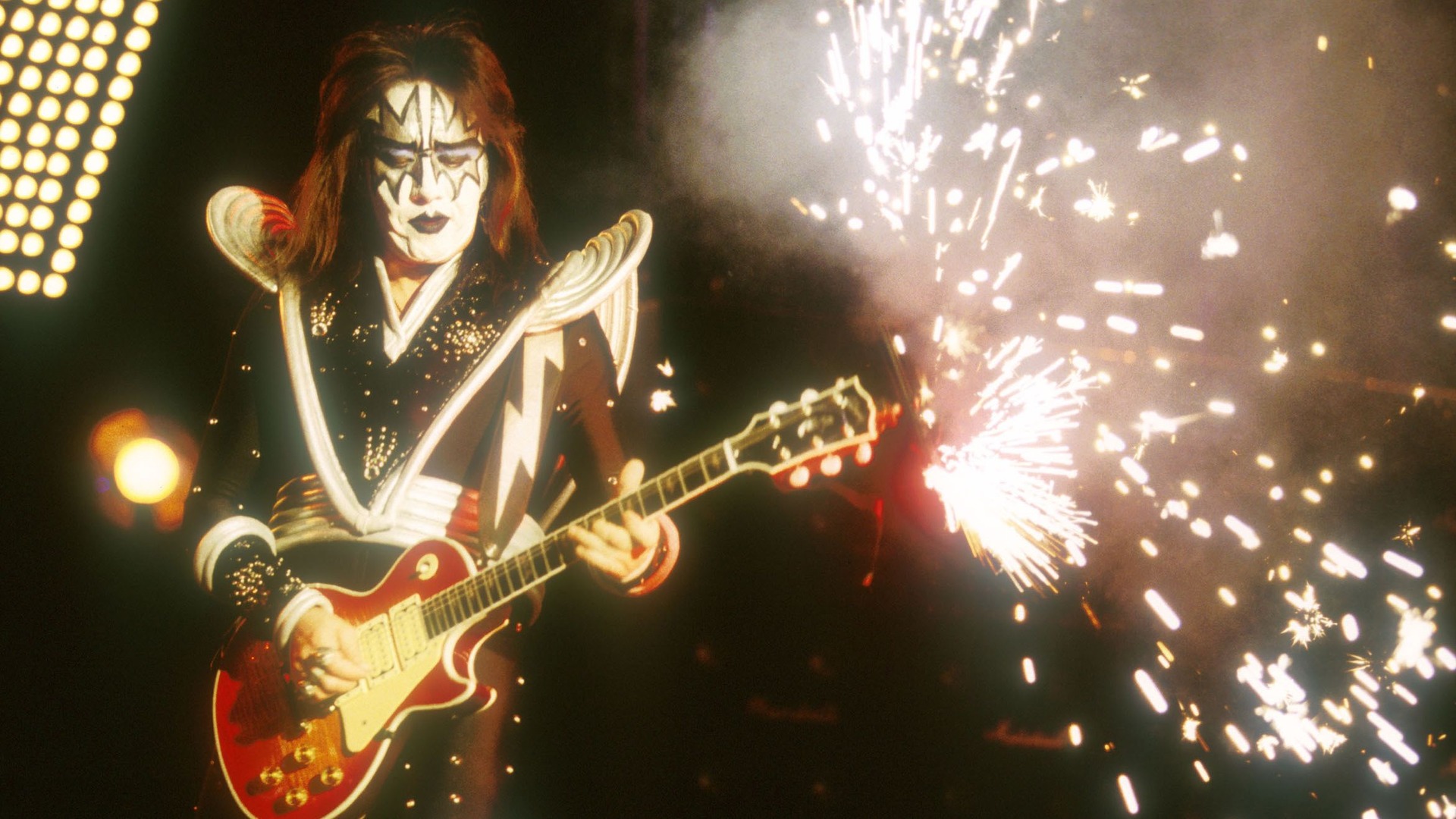 Ace Frehley tocando guitarra durante show do Kiss, com fogos de artifício no palco.