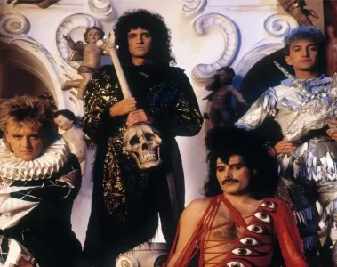 Queen em registro promocional nos anos 80, com Freddie Mercury, Brian May, Roger Taylor e John Deacon usando figurinos teatrais e posando em cenário barroco. Foto: Queen Productions Ltd.