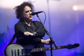 Robert Smith, vocalista e guitarrista do The Cure, se apresenta ao vivo em show com guitarra em mãos.
