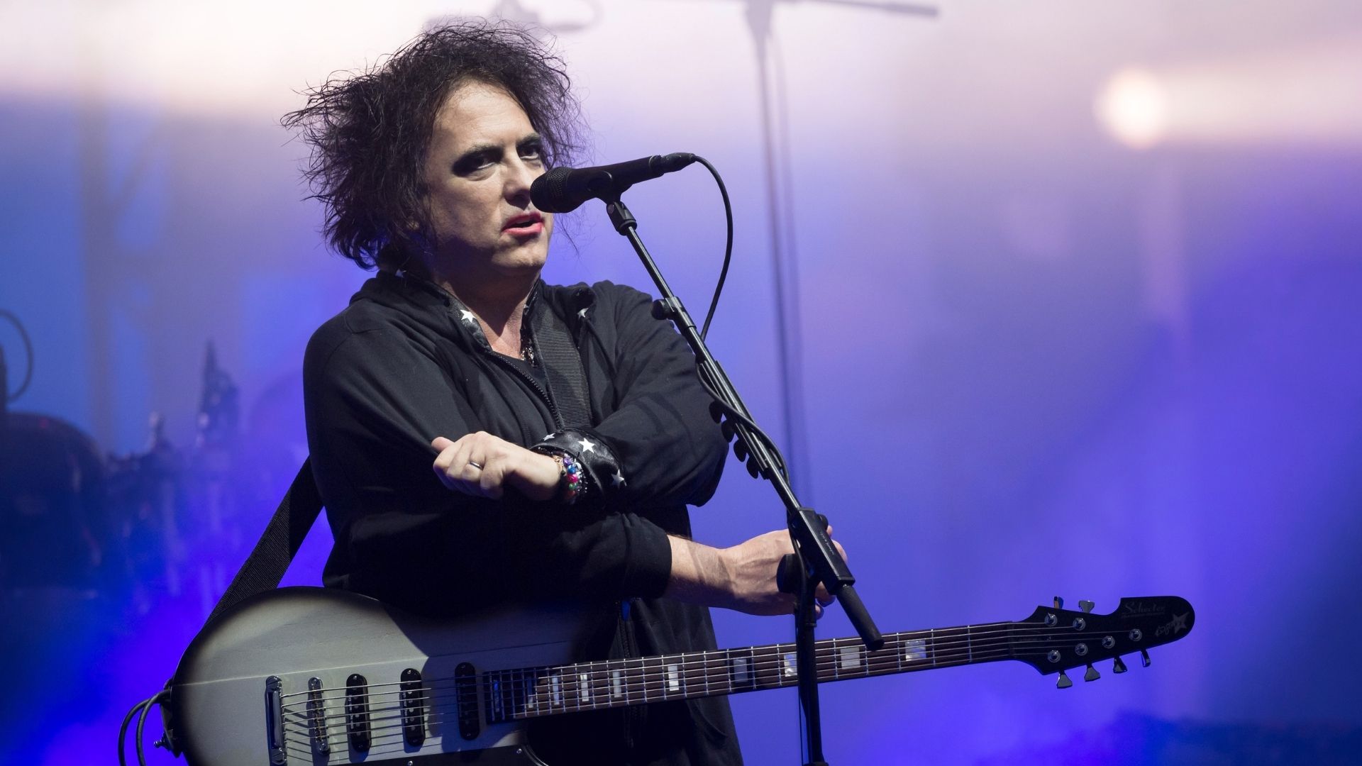 Robert Smith, vocalista e guitarrista do The Cure, se apresenta ao vivo em show com guitarra em mãos.