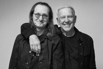 Geddy Lee e Alex Lifeson, do Rush, sorrindo e abraçados para anunciar a turnê Fifty-Something de 2026.
