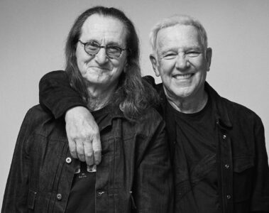 Geddy Lee e Alex Lifeson, do Rush, sorrindo e abraçados para anunciar a turnê Fifty-Something de 2026.