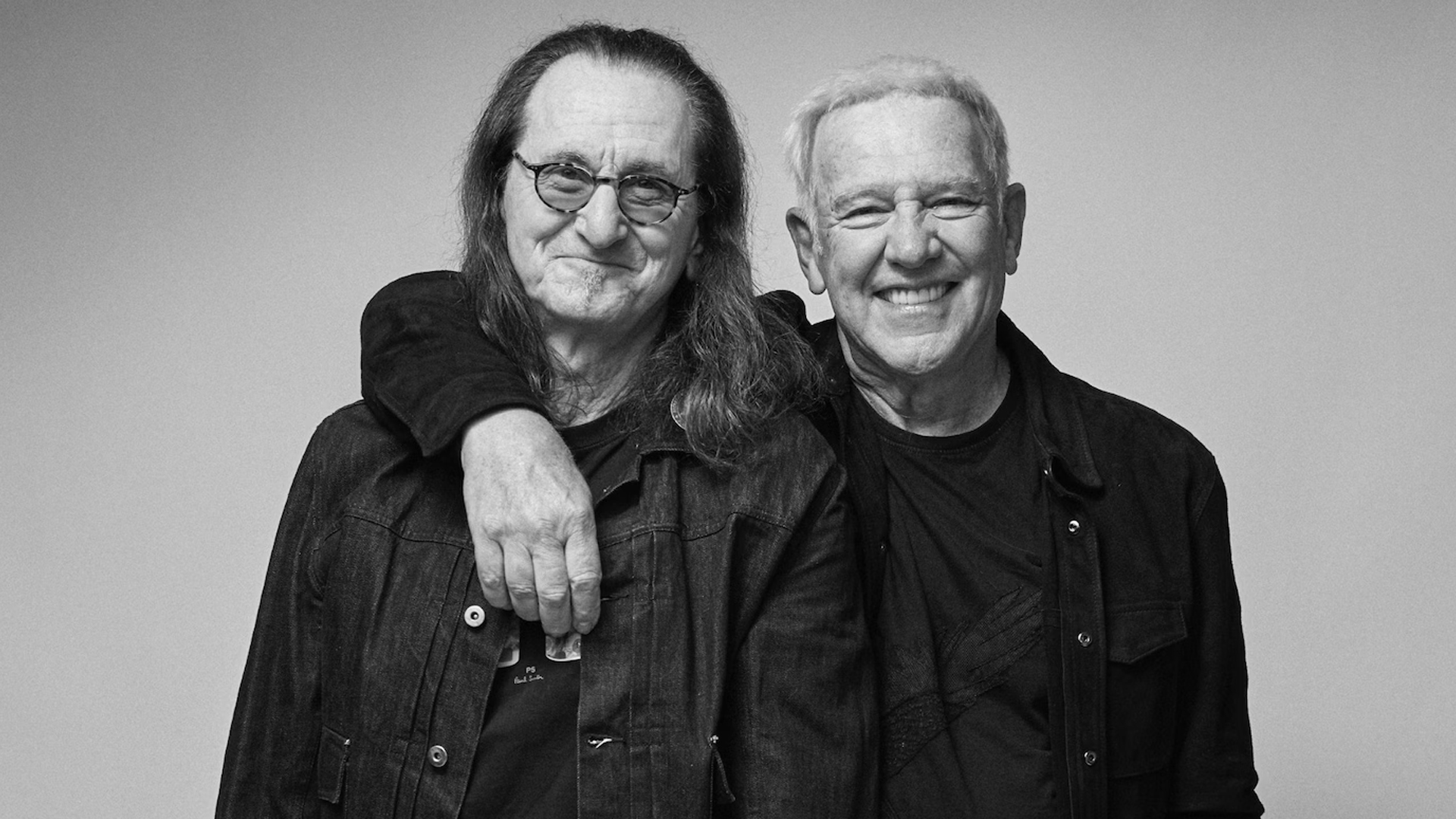 Geddy Lee e Alex Lifeson, do Rush, sorrindo e abraçados para anunciar a turnê Fifty-Something de 2026.