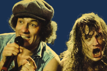 Brian Johnson e Angus Young do AC/DC durante apresentação ao vivo, com expressões intensas e iluminação dramática.