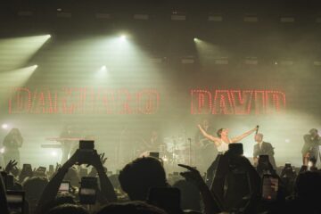 Damiano David se apresenta no palco do Tokyo Marine Hall em São Paulo durante sua turnê solo FUNNY Little FEARS, com luzes douradas e o público vibrando.