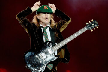 Angus Young, guitarrista do AC/DC, fazendo sua pose clássica com uma Gibson SG durante show ao vivo.