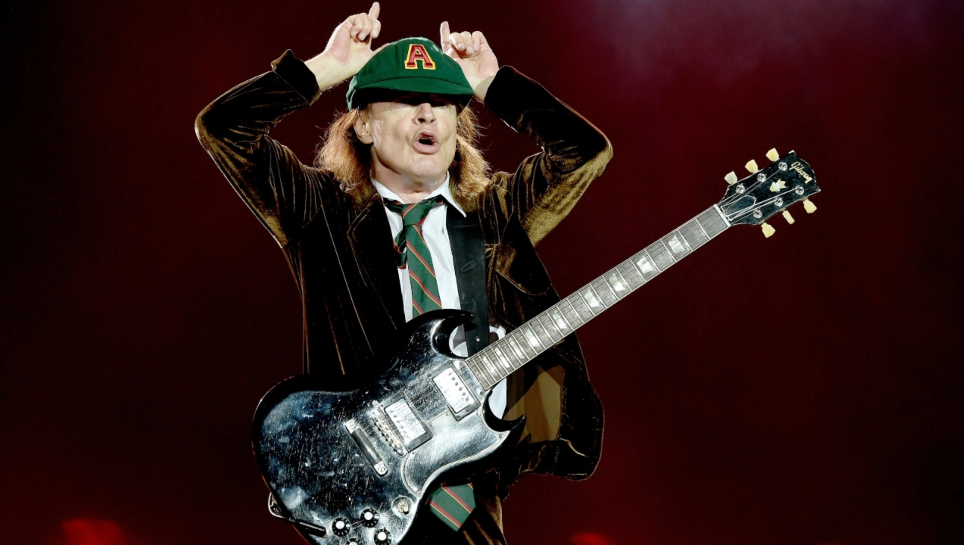 Angus Young, guitarrista do AC/DC, fazendo sua pose clássica com uma Gibson SG durante show ao vivo.