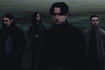 Foto escura e atmosférica do Bad Omens em um campo enevoado, com os quatro integrantes posando de forma séria, em tons frios e clima melancólico.