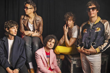 Foto do The Strokes posando juntos; Julian Casablancas e o guitarrista Nick Valensi aparecem com os outros integrantes em um estúdio.