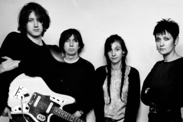 Foto em preto e branco do My Bloody Valentine em 1990, com Kevin Shields segurando uma guitarra ao lado dos outros integrantes. Crédito: Steve Gullick.