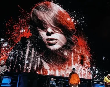 Oasis no palco em São Paulo com imagem de Mani Mounfield em vermelho e branco exibida no telão durante homenagem.