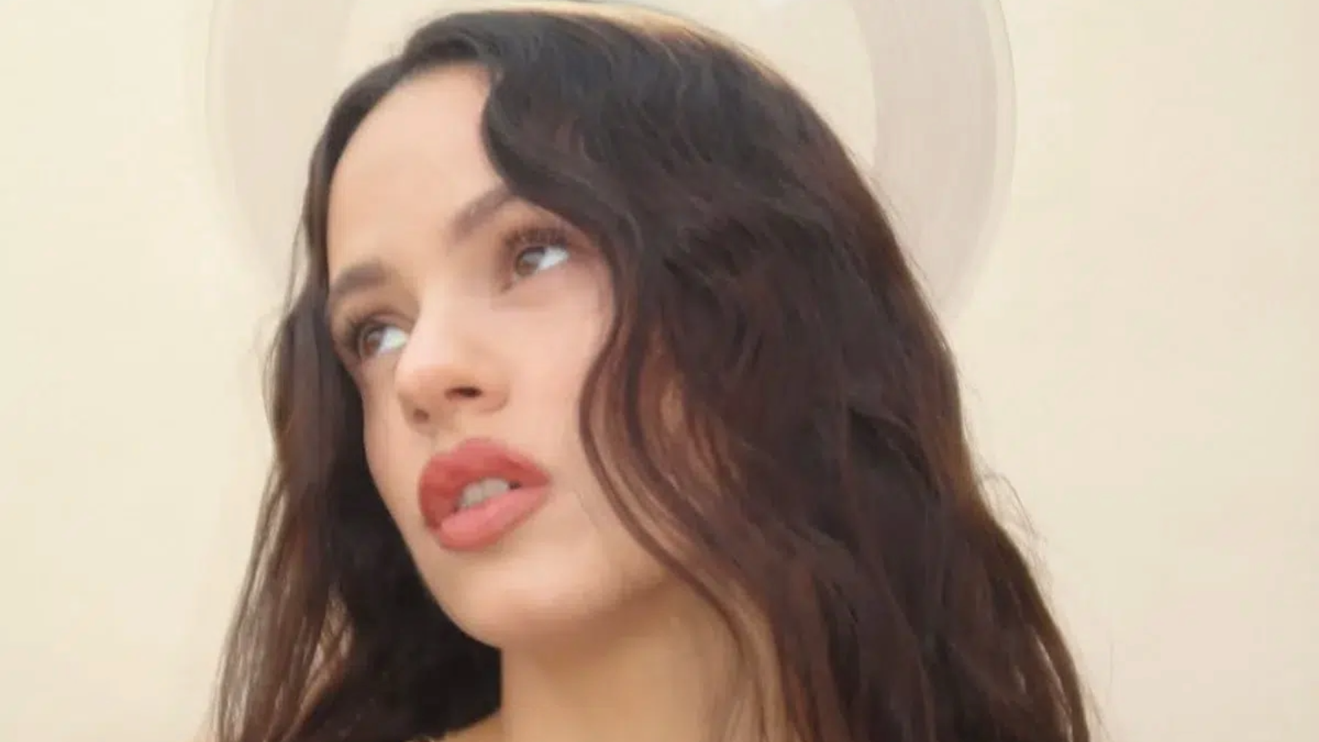 Rosalía em close-up com expressão contemplativa e efeito visual que remete a um halo, representando o conceito espiritual do álbum “Lux”.