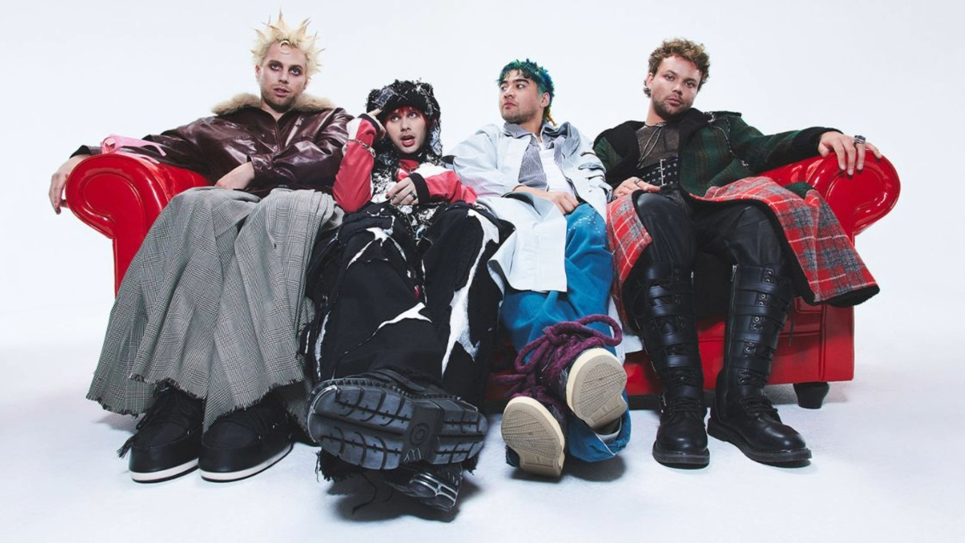 Integrantes do 5 Seconds of Summer sentados em um sofá vermelho em ensaio fotográfico promocional.
