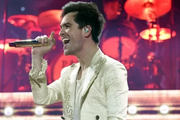 Brendon Urie canta em show do Panic! At The Disco segurando microfone dourado, com luzes vermelhas ao fundo — Foto: Tim Mosenfelder/WireImage.