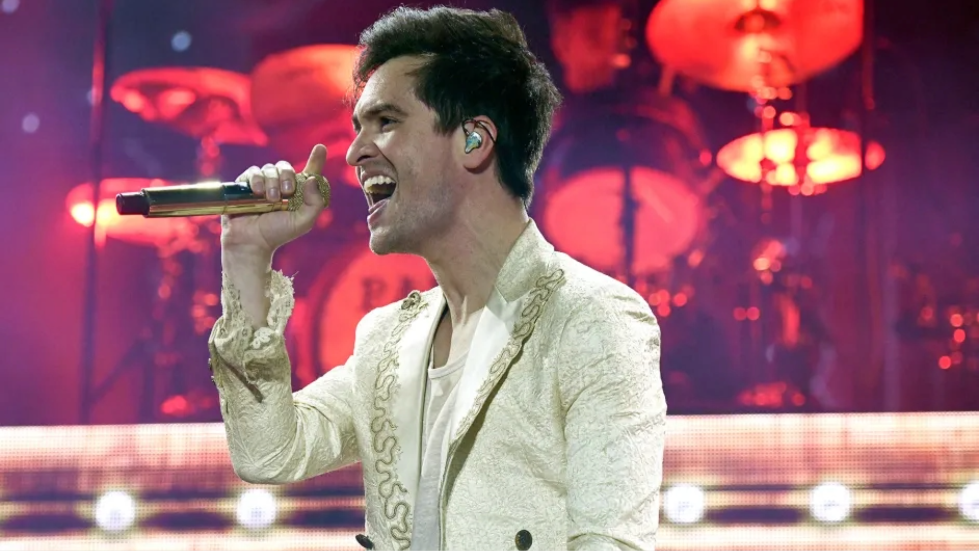 Brendon Urie canta em show do Panic! At The Disco segurando microfone dourado, com luzes vermelhas ao fundo — Foto: Tim Mosenfelder/WireImage.