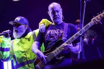 Fred Durst homenageia o baixista Sam Rivers durante show do Limp Bizkit na Cidade do México, com o vocalista apoiando o braço no colega enquanto ele toca baixo sob luzes roxas do palco.
