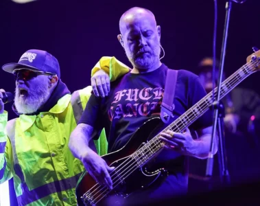 Fred Durst homenageia o baixista Sam Rivers durante show do Limp Bizkit na Cidade do México, com o vocalista apoiando o braço no colega enquanto ele toca baixo sob luzes roxas do palco.