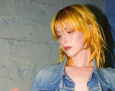 Hayley Williams com cabelo amarelo dourado olhando para baixo em um ambiente urbano.