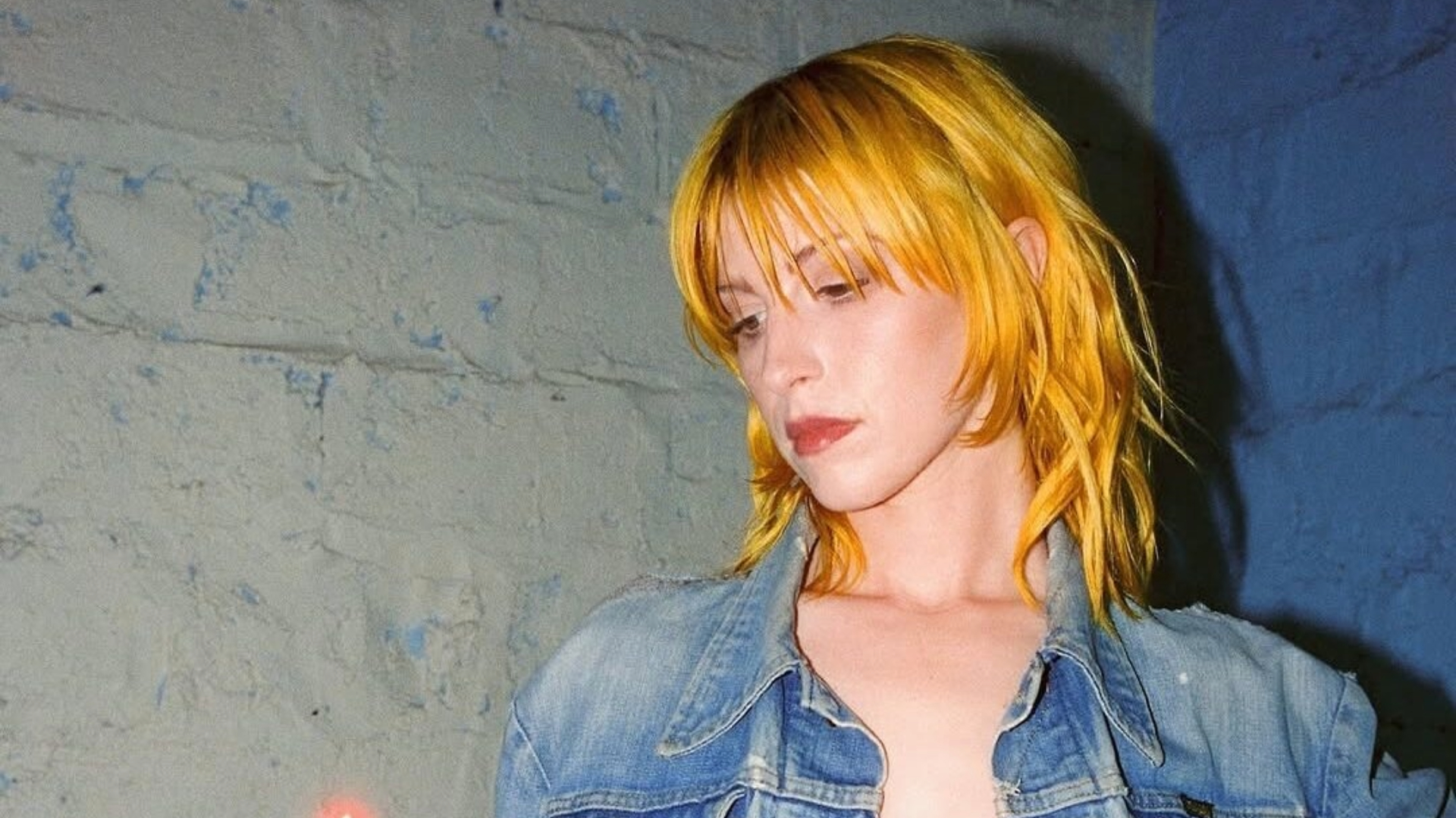 Hayley Williams com cabelo amarelo dourado olhando para baixo em um ambiente urbano.