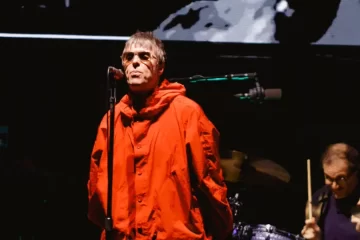 Liam Gallagher usa parka vermelha e canta em frente ao microfone durante show do Oasis em São Paulo.Liam Gallagher durante o último show do Oasis em São Paulo, no Allianz Parque, durante a turnê “Live ’25”. (Foto: Patrícia Devoraes / Brazil News)