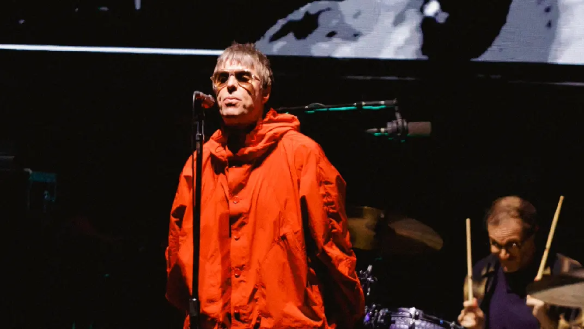 Liam Gallagher usa parka vermelha e canta em frente ao microfone durante show do Oasis em São Paulo.Liam Gallagher durante o último show do Oasis em São Paulo, no Allianz Parque, durante a turnê “Live ’25”. (Foto: Patrícia Devoraes / Brazil News)