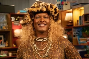 Liniker sorrindo em estúdio do Tiny Desk Brasil, usando chapéu e roupa com estampa animal print, durante gravação do episódio com música inédita.