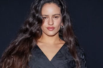 Rosalía posando com look preto em fundo escuro antes da turnê LUX 2026.