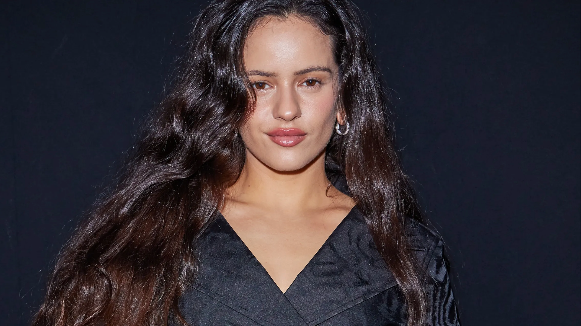 Rosalía posando com look preto em fundo escuro antes da turnê LUX 2026.