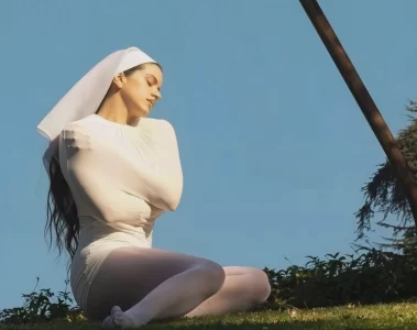Rosalía sentada em um gramado, vestindo figurino branco, em imagem promocional do álbum “LUX”.