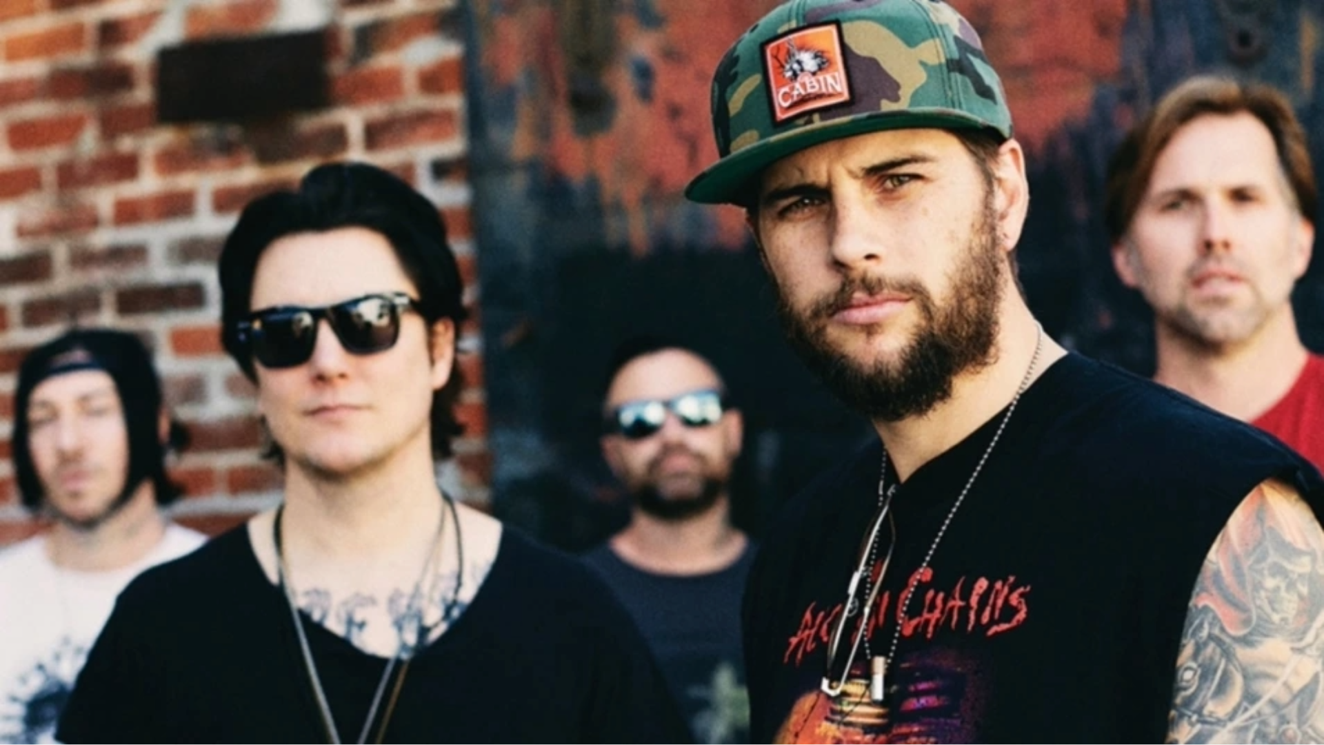 Banda Avenged Sevenfold posando ao ar livre, com M. Shadows em destaque usando boné camuflado.